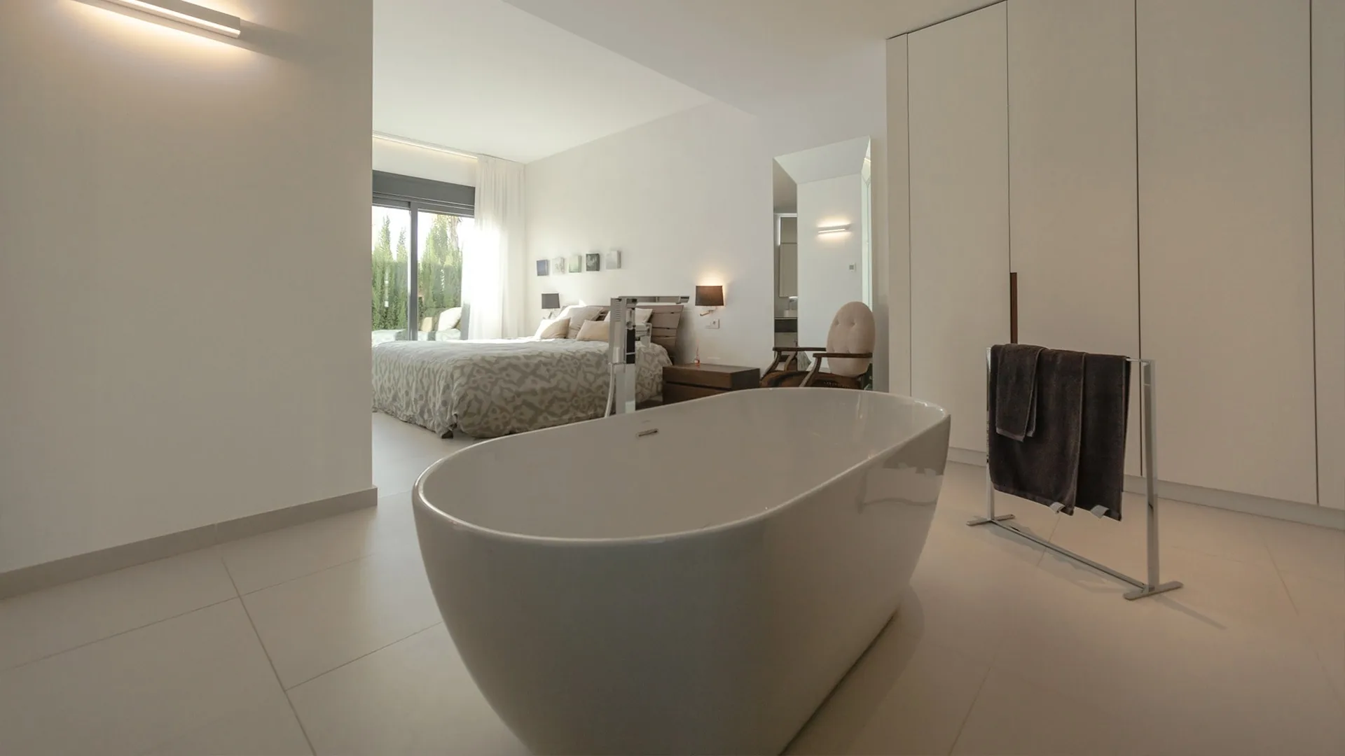 Moderne en-suite badkamer met vrijstaand bad, stucwerk en grote lichte vloertegels