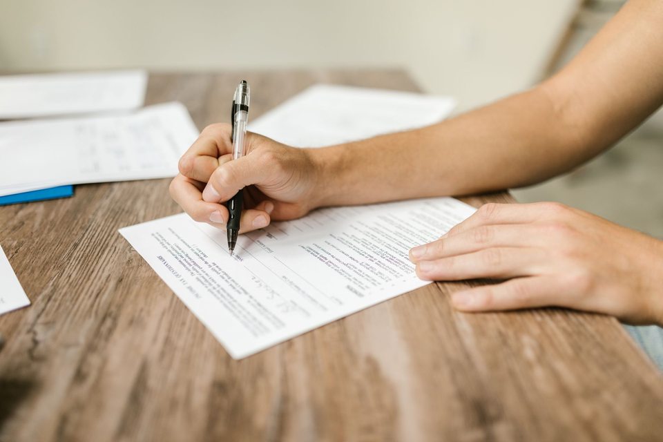 Handen die aan een houten tafel een document invullen.