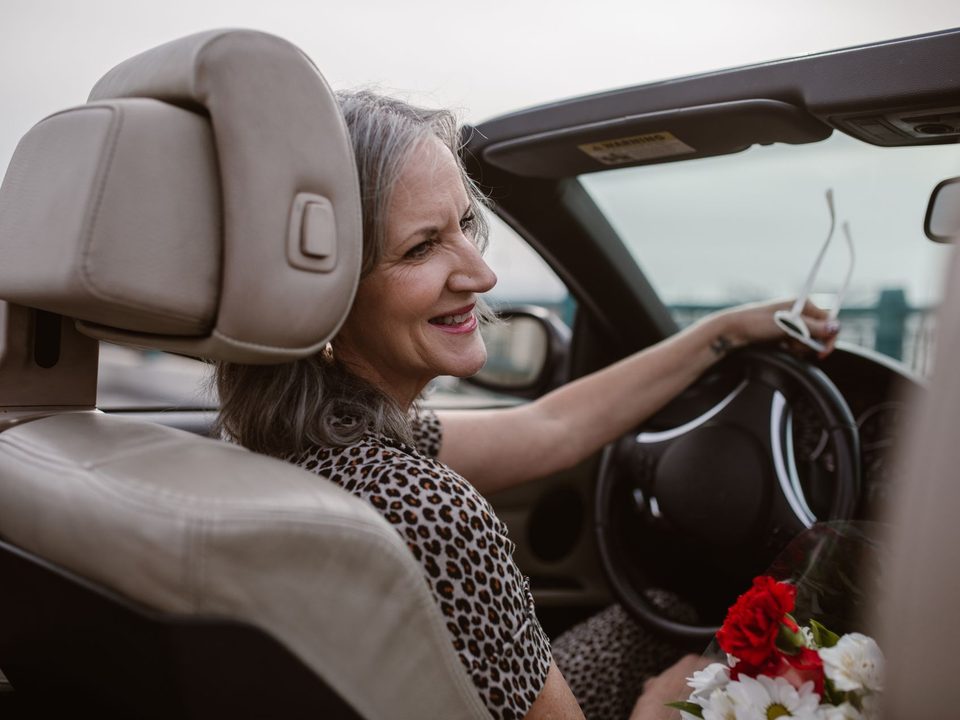 Een oudere vrouw zit ontspannen achter het stuur van haar auto.